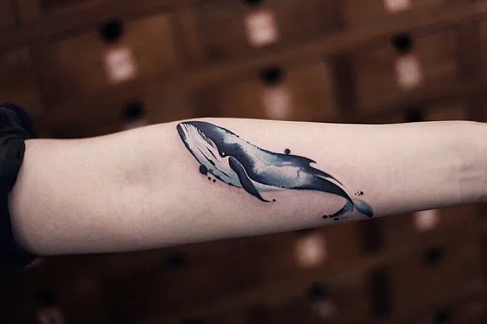 Watercolor tattoo of a blue whale on an arm by Chen Jie.