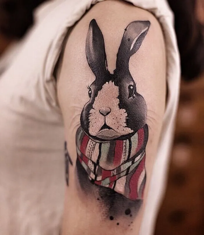 Watercolor tattoo of a rabbit with a colorful scarf on an upper arm, created by artist Chen Jie.