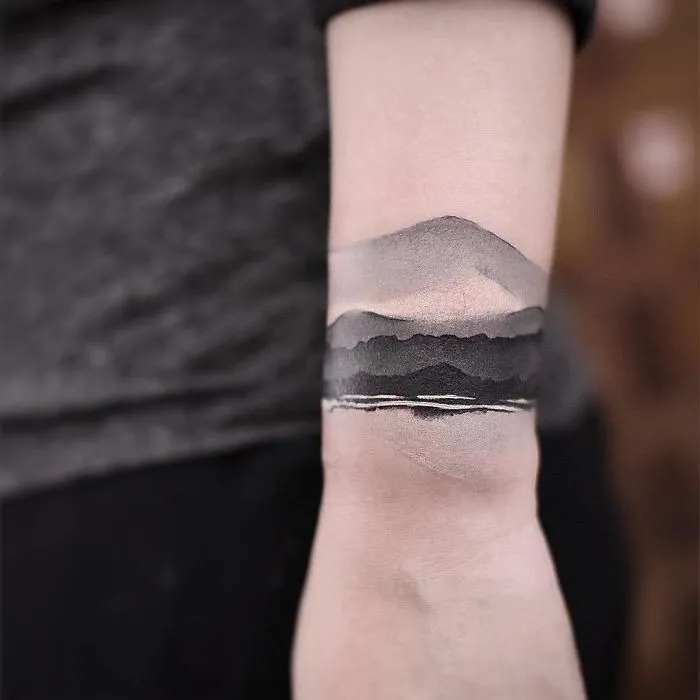 Watercolor tattoo by Chen Jie on an arm, featuring a serene mountain and landscape scene.
