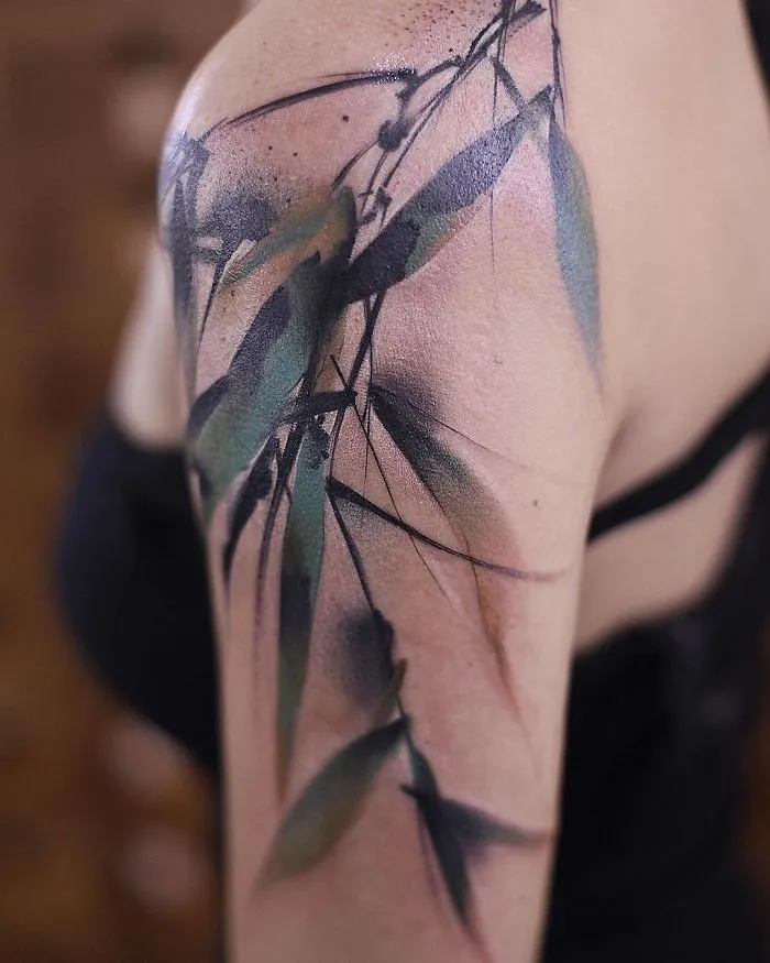 Watercolor tattoo on a shoulder, featuring abstract floral design with green and purple hues.