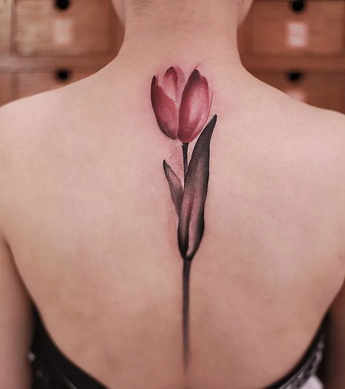Watercolor tattoo of a pink flower on a person's upper back, showcasing Chen Jie's artistry.