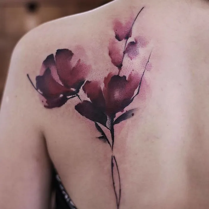 Watercolor tattoo depicting delicate red flowers on a person's back, showcasing Chen Jie's artistic style.
