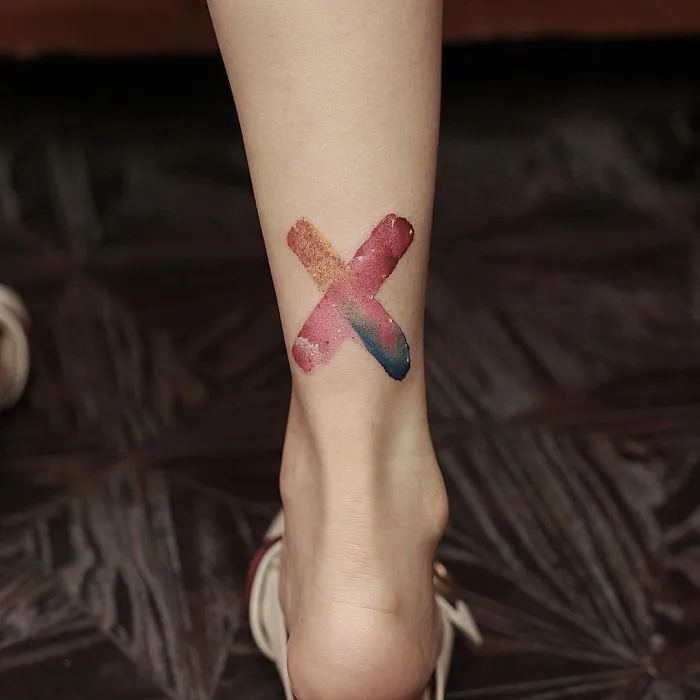 Watercolor tattoo on ankle featuring an abstract X design by Chen Jie.