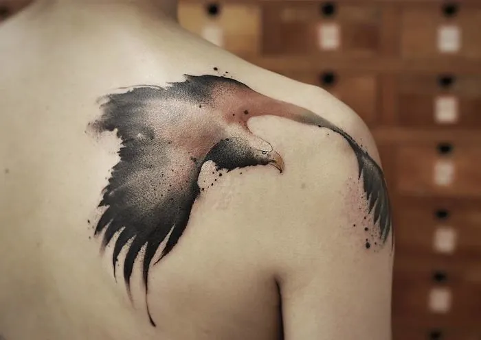 Watercolor tattoo of an eagle on a person's back, featuring fluid brushstrokes and soft color blending.