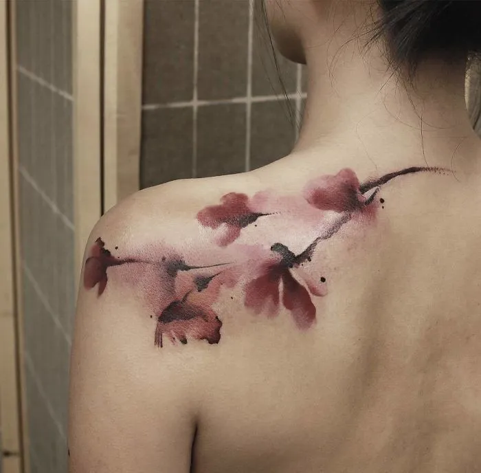Watercolor tattoo of pink flowers on a woman's shoulder, showcasing Chen Jie's artistic style.