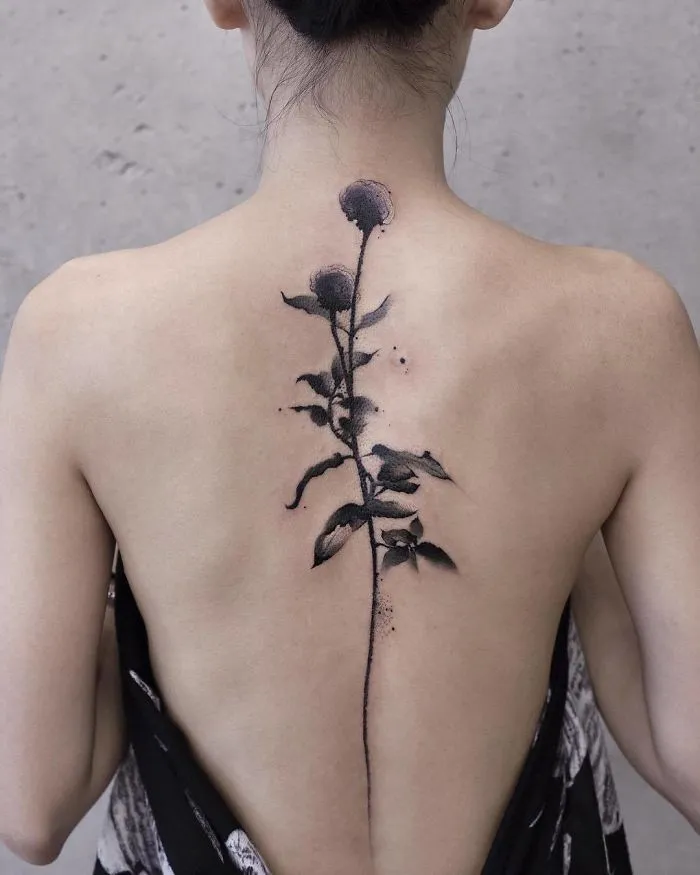 Watercolor tattoo of a delicate flower design on a person's back.