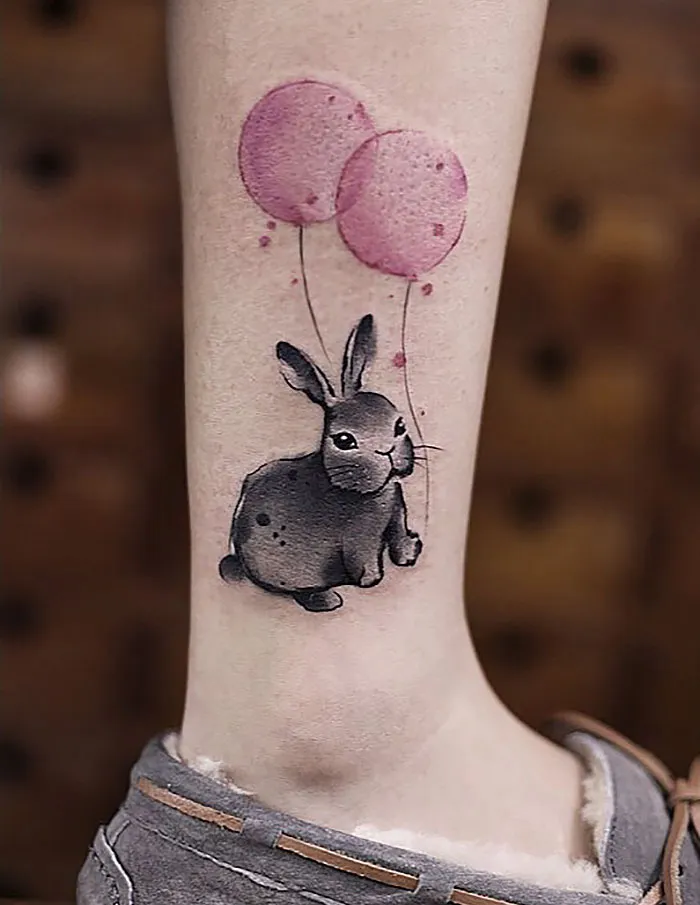 Watercolor tattoo of a gray rabbit with pink balloons on a person's leg.
