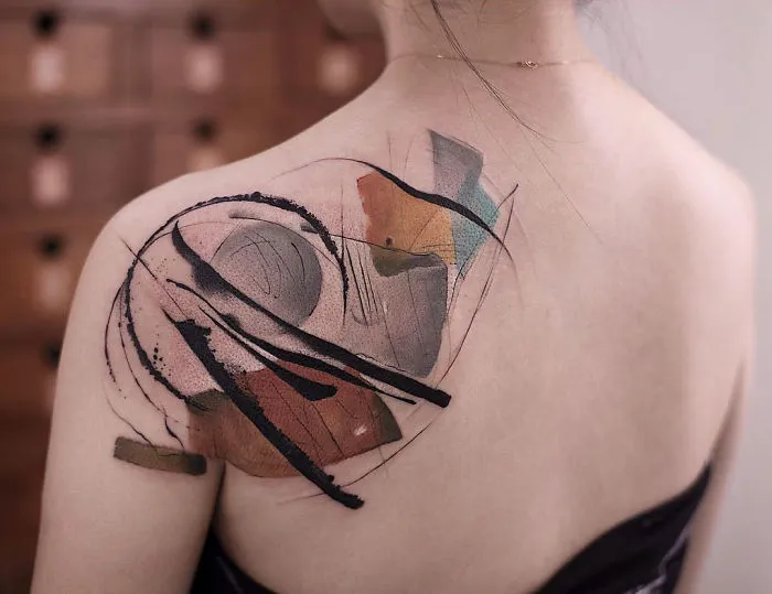 Watercolor tattoo by Chen Jie on a woman's shoulder, featuring abstract brush strokes and colorful shapes.