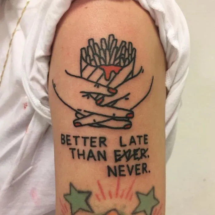 Irreverent tattoo of hands holding fries with text "Better late than never" on arm.