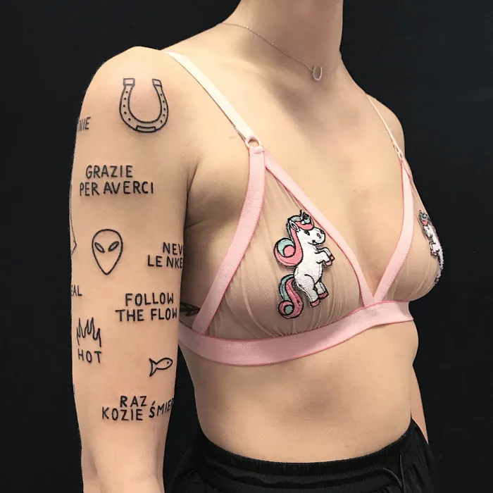 Irreverent tattoos on a woman's arm and torso, featuring phrases, symbols, and a unicorn design.