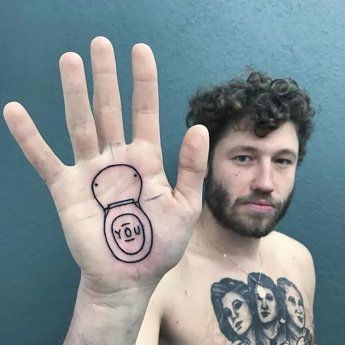Man showing a unique tattoo of a toilet seat on his palm, created by a German tattoo artist.