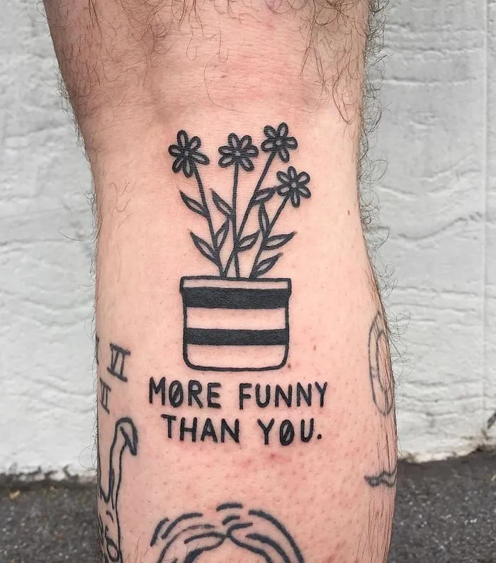 Irreverent tattoo by German artist featuring potted flowers with the text "more funny than you" on a person's leg.