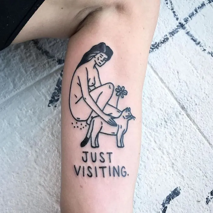 Irreverent tattoo by a German artist featuring a woman with a cat and the phrase "Just Visiting" on an arm.