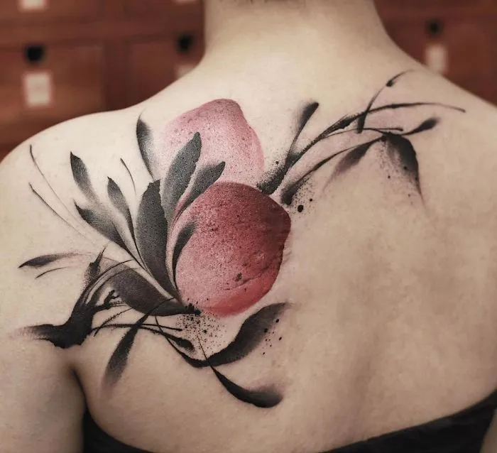 Watercolor tattoo on upper back with floral and abstract design, featuring pink and black hues.