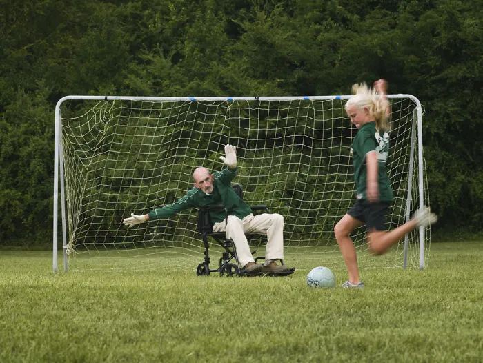 Girl playing soccer with grandfather in wheelchair as goalkeeper