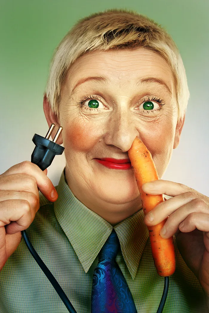 Happy short hair woman with green eyes putting an electric carrot into her nose and holding a power cord in other