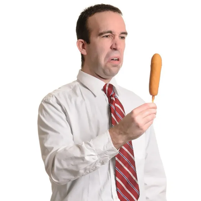 Man in a white shirt and red tie is disgusted by corndog