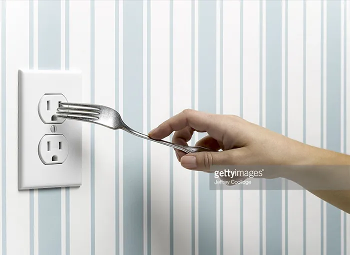 Hand putting a fork into the electric outlet