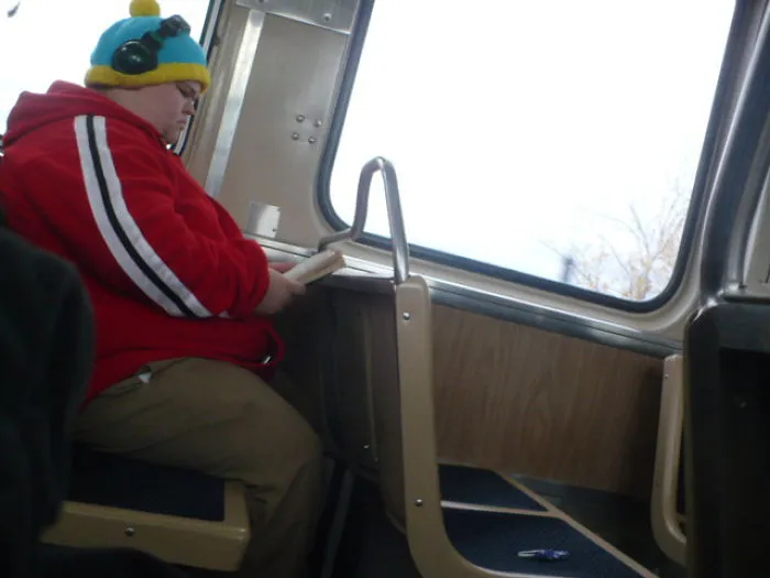 Person in red jacket and colorful hat reading on a train, resembling accidental cosplay.