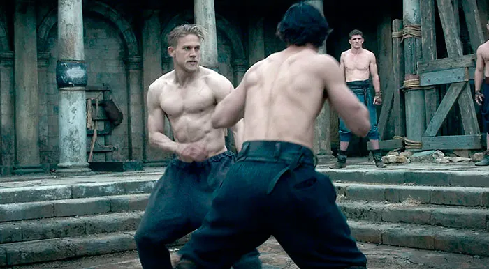 Two shirtless men fighting in a courtyard scene from King Arthur Legend Of The Sword for fun facts about movies.
