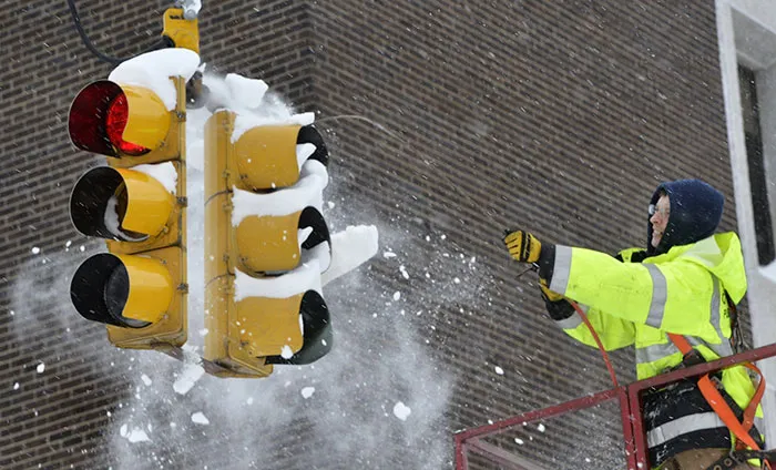 Empleado de tráfico en Erie usando aire comprimido para quitar nieve y hielo del semáforo