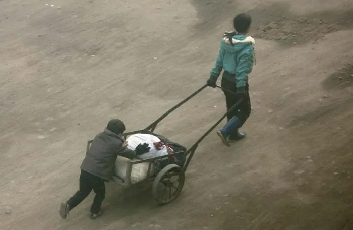 Two kids carrying a stroller with bags 