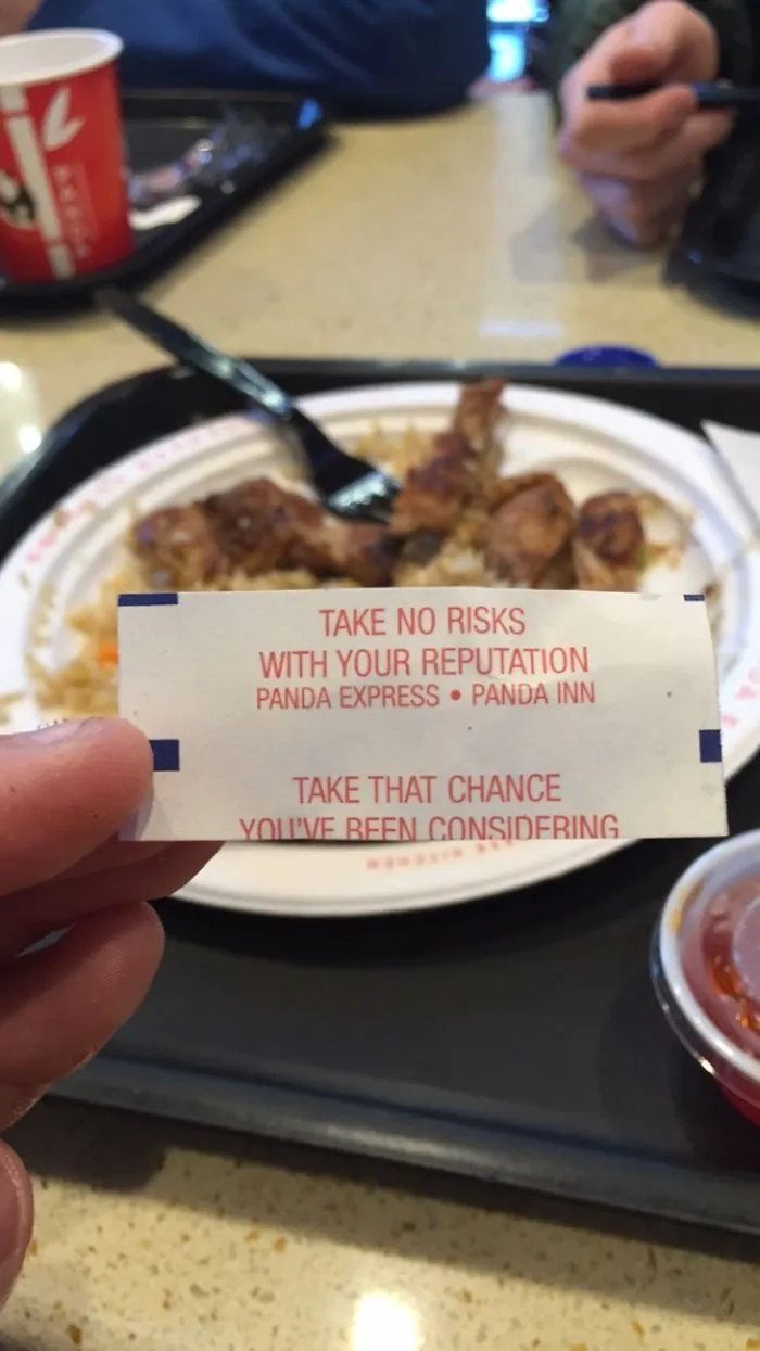 Fortune cookie on tray with a sassy message about taking risks, plate of food in background.