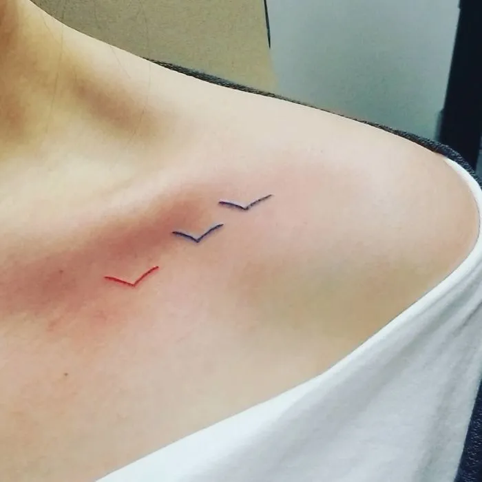 Minimal bird tattoos in blue, purple, and red ink on shoulder, symbolizing stories behind tattoos with real meaning.