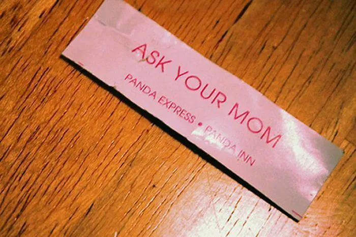 Fortune cookie saying with a sassy message: "Ask Your Mom" on a wooden table.