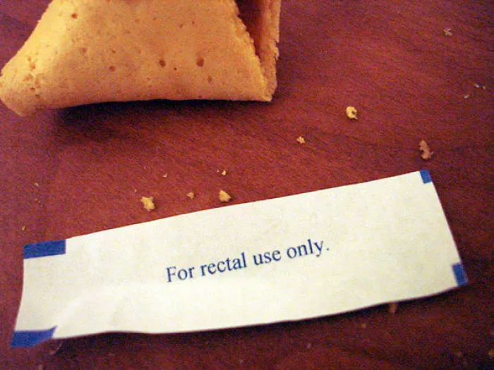 Fortune cookie with a humorous message: "For rectal use only" on a wooden surface.