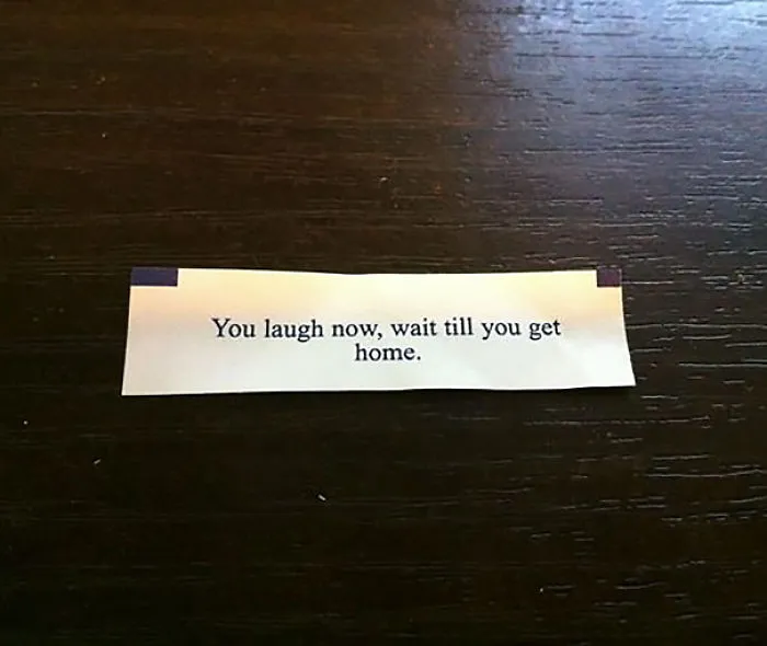 Fortune cookie saying: "You laugh now, wait till you get home" on a wooden table.