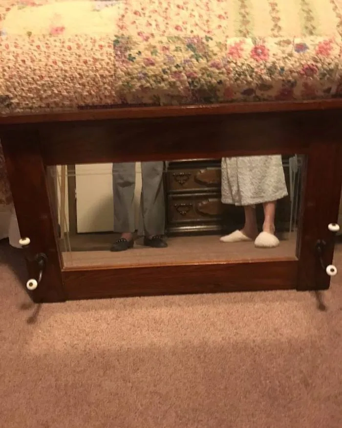 People's feet reflected in a mirror for sale, placed under a quilted cover.