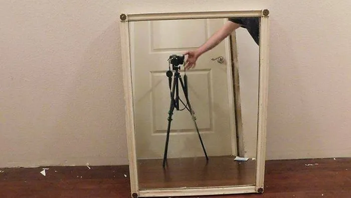 Person's arm adjusting camera tripod reflected in a framed mirror for sale, highlighting the challenge of selling mirrors.