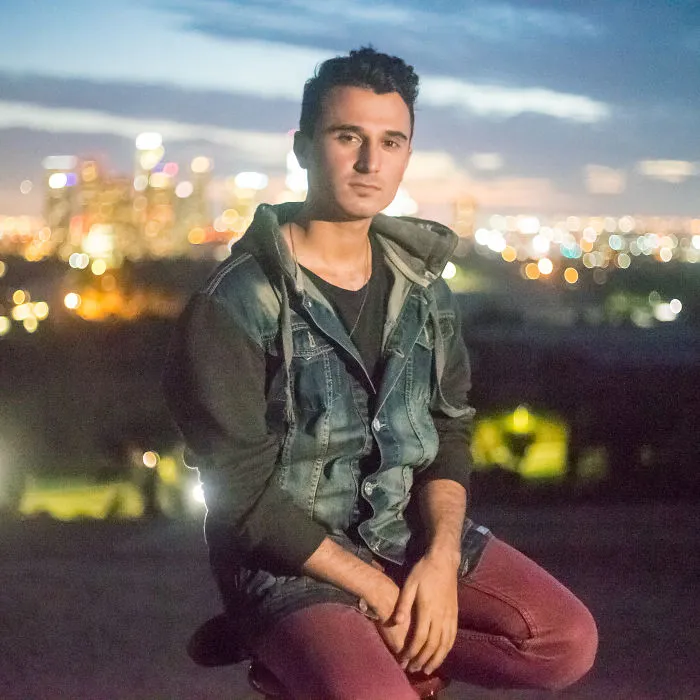 Young man posing outdoors at dusk with city lights in the background, featuring interviews on birthdays concept.