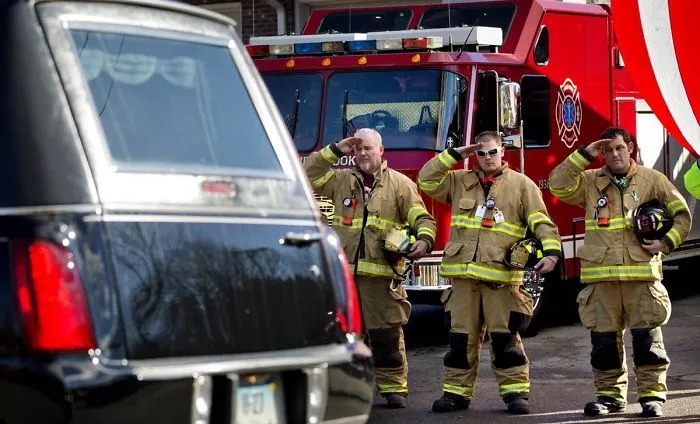 Bomberos saludando en la procesión del funeral de una víctima de 7 años de un tiroteo en una escuela