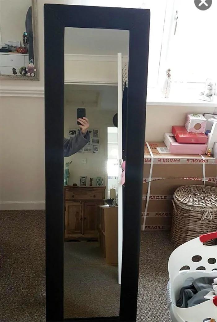 Person taking a photo of a large mirror in a room, showing part of their arm.