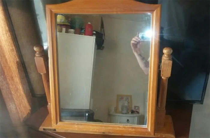 A person taking a photo in a wooden framed mirror for sale.