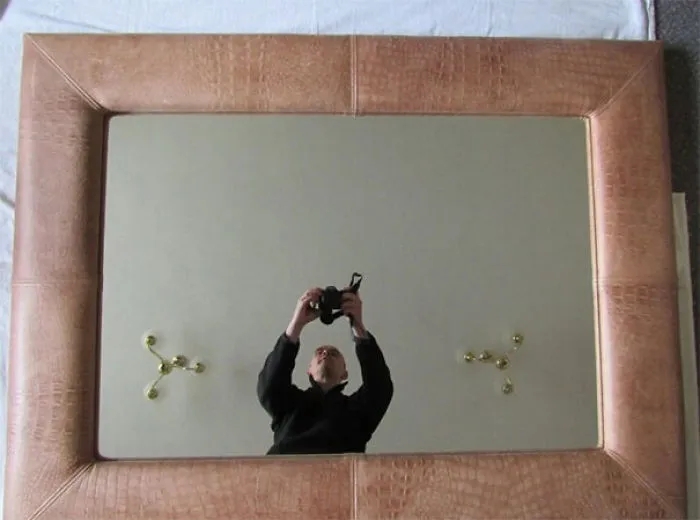 Person taking a photo of a large mirror with a brown frame from below.