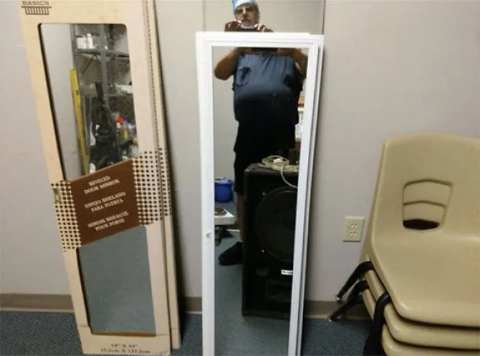 Person taking a photo of a mirror for sale, reflection showing part of the room including chairs and cardboard packaging.