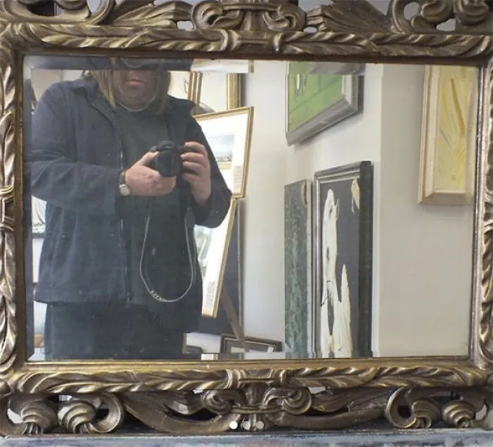 Person taking photo in a mirror, capturing reflection in ornate frame, related to selling mirrors.