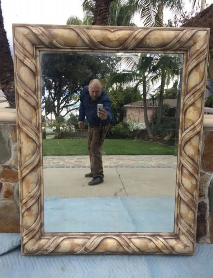 Person taking a selfie in a large ornate mirror, showcasing its decorative frame.
