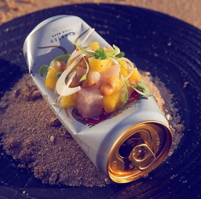 Pescado servido en una lata de cerveza vacía sobre un cenicero sucio