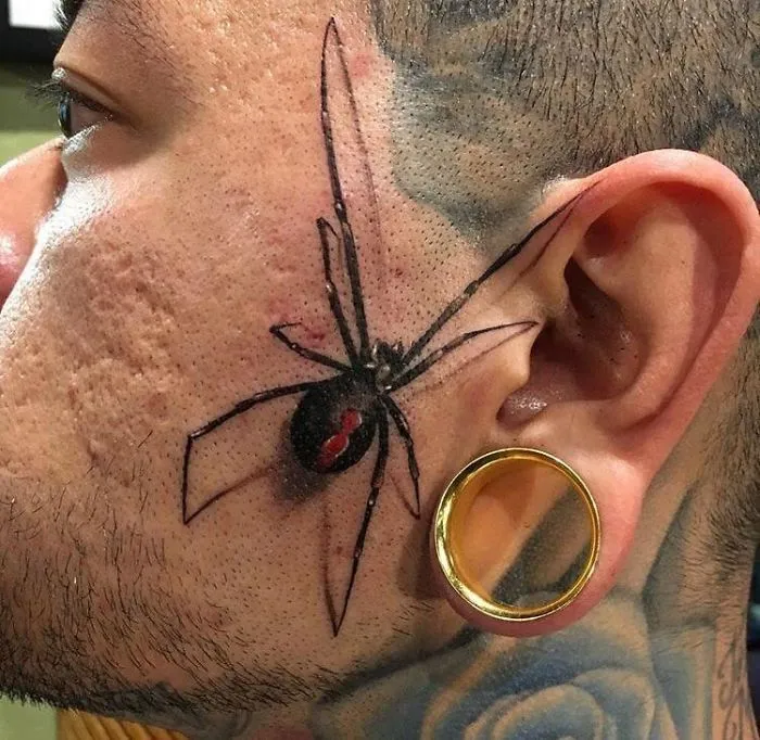 Spider tattoo fail on man's cheek near ear with gauged earring.