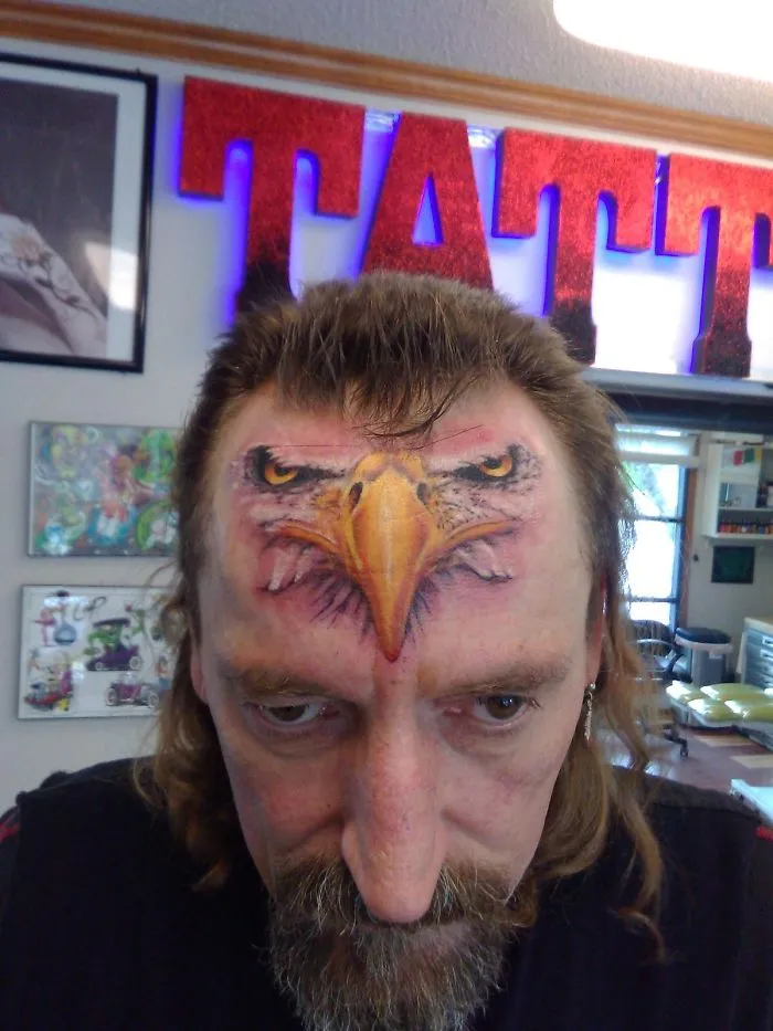 Man with an eagle tattoo on his forehead inside a tattoo parlor; a humorous and cringe-worthy tattoo fail.