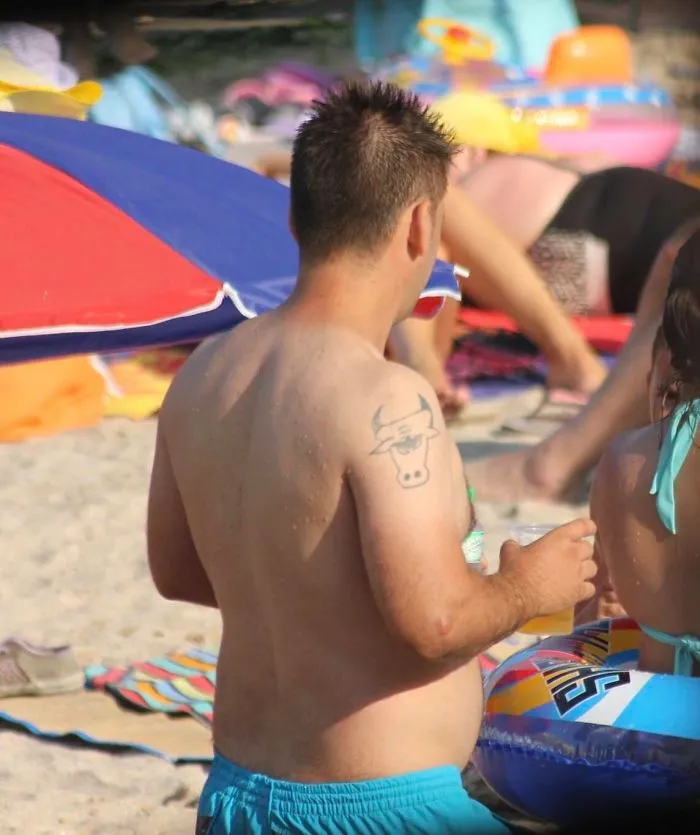Man with a comical bull tattoo on shoulder at the beach, showcasing a tattoo fail.