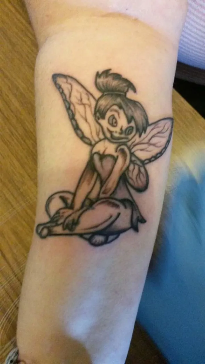Fairy tattoo fail with awkward expression and uneven lines on forearm.