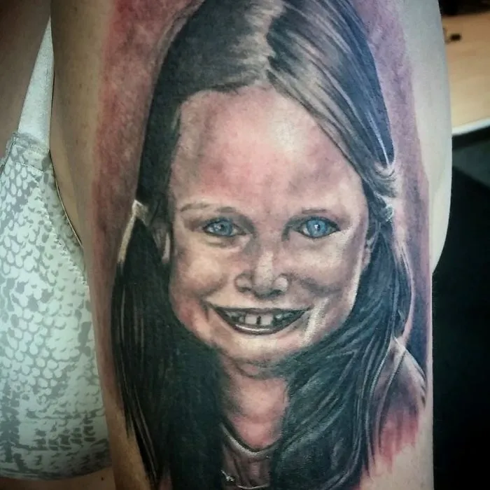 A portrait tattoo fail depicting a child's face with a distorted smile.