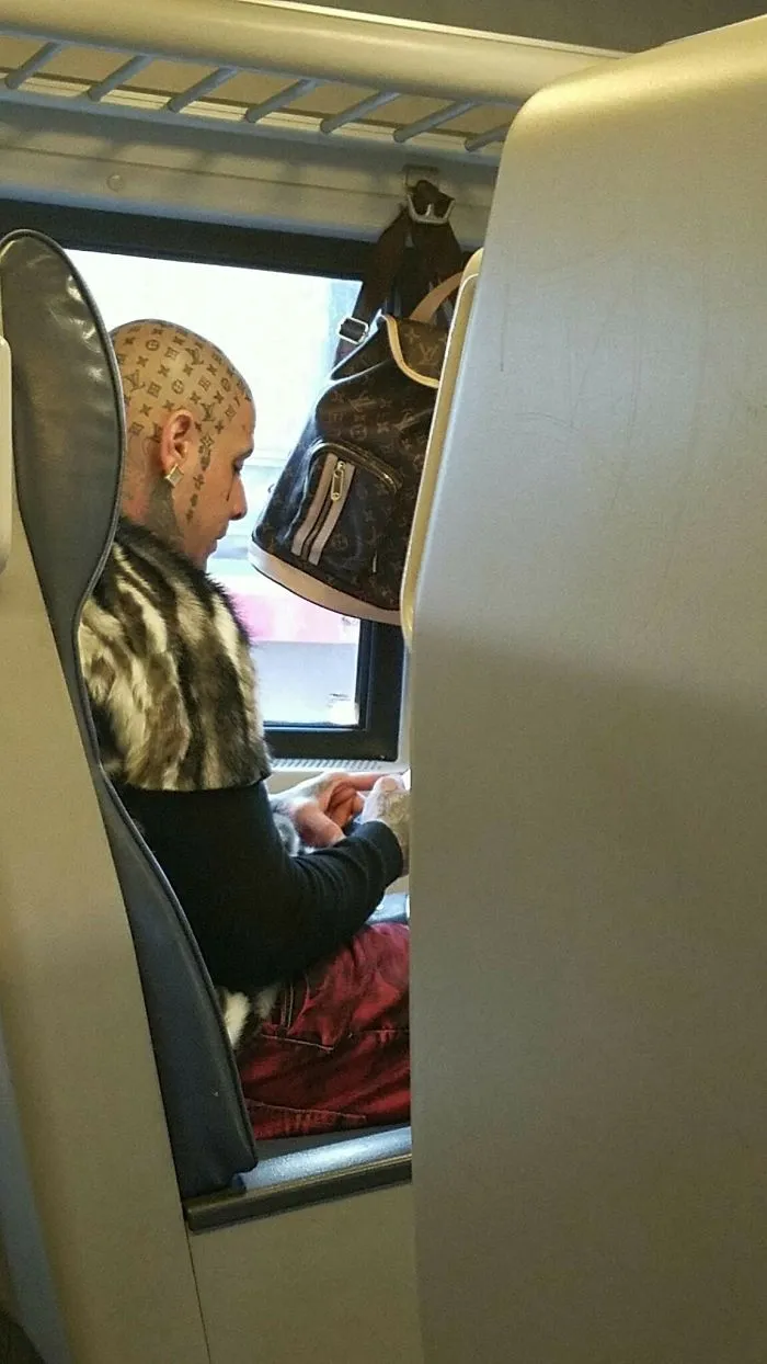 Person with unusual head tattoos sitting on a train, showcasing a bad tattoo fail that’s both laughable and cringe-worthy.