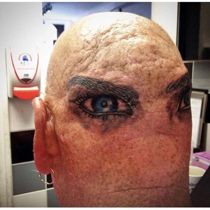 Bald head with poorly tattooed eyes, humorous tattoo fail.