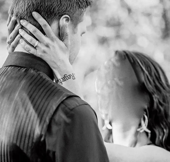 Couple embracing, woman's hand shows tattoo fail, with fading black ink on wrist, adding a humorous element.